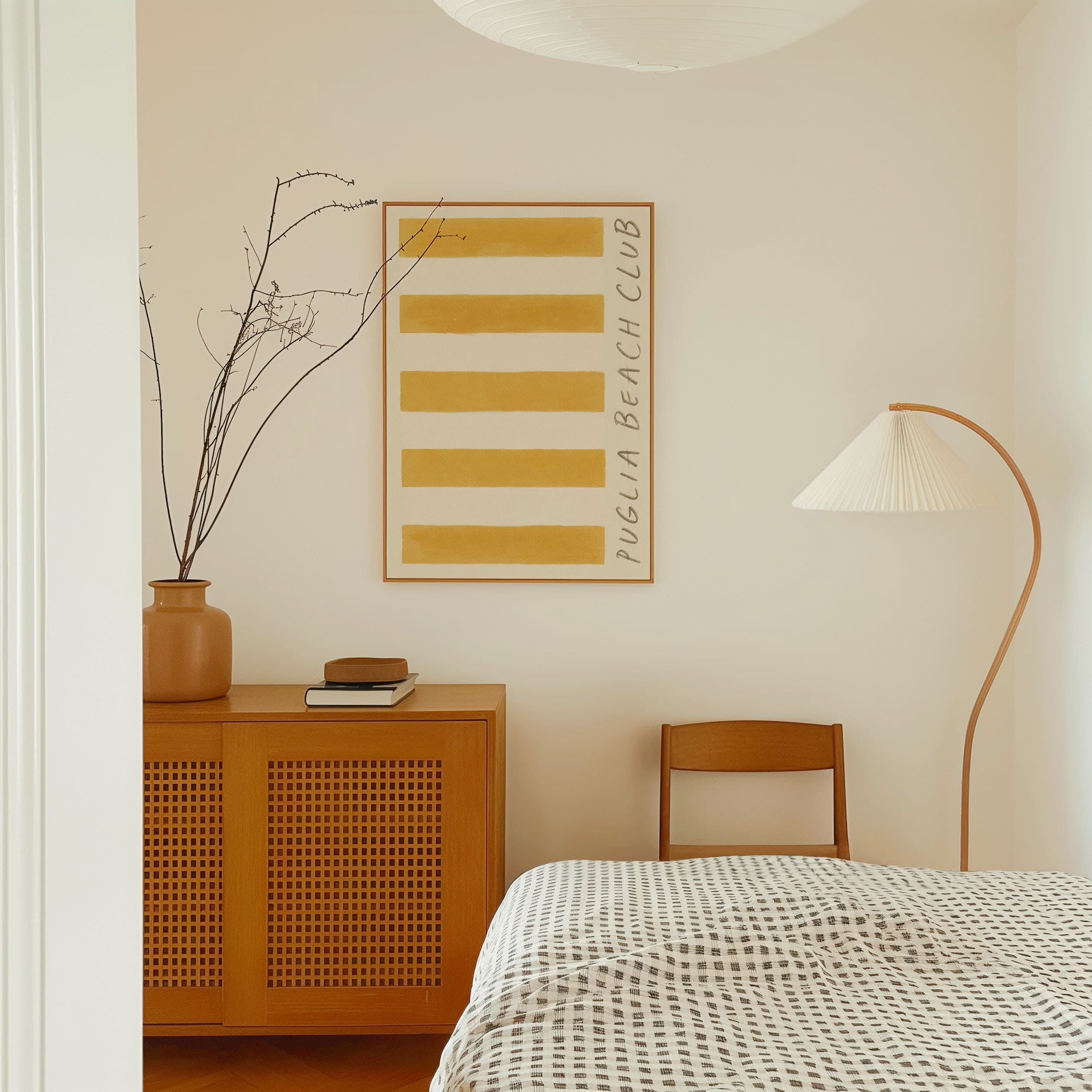 Puglia beach club stripe giclee art print of original artist oil painting in a rich deep ochre yellow. This artwork by Falmouth artist Mads is a replica of a retro stripe beach towel. In this photograph, the cotton paper puglia beach art print hangs in a thin oak frame on off-white painted bedroom wall. Paint colour by Atelier Ellis. The art is displayed in a modern bedroom with European styling and Scandinavian accents.