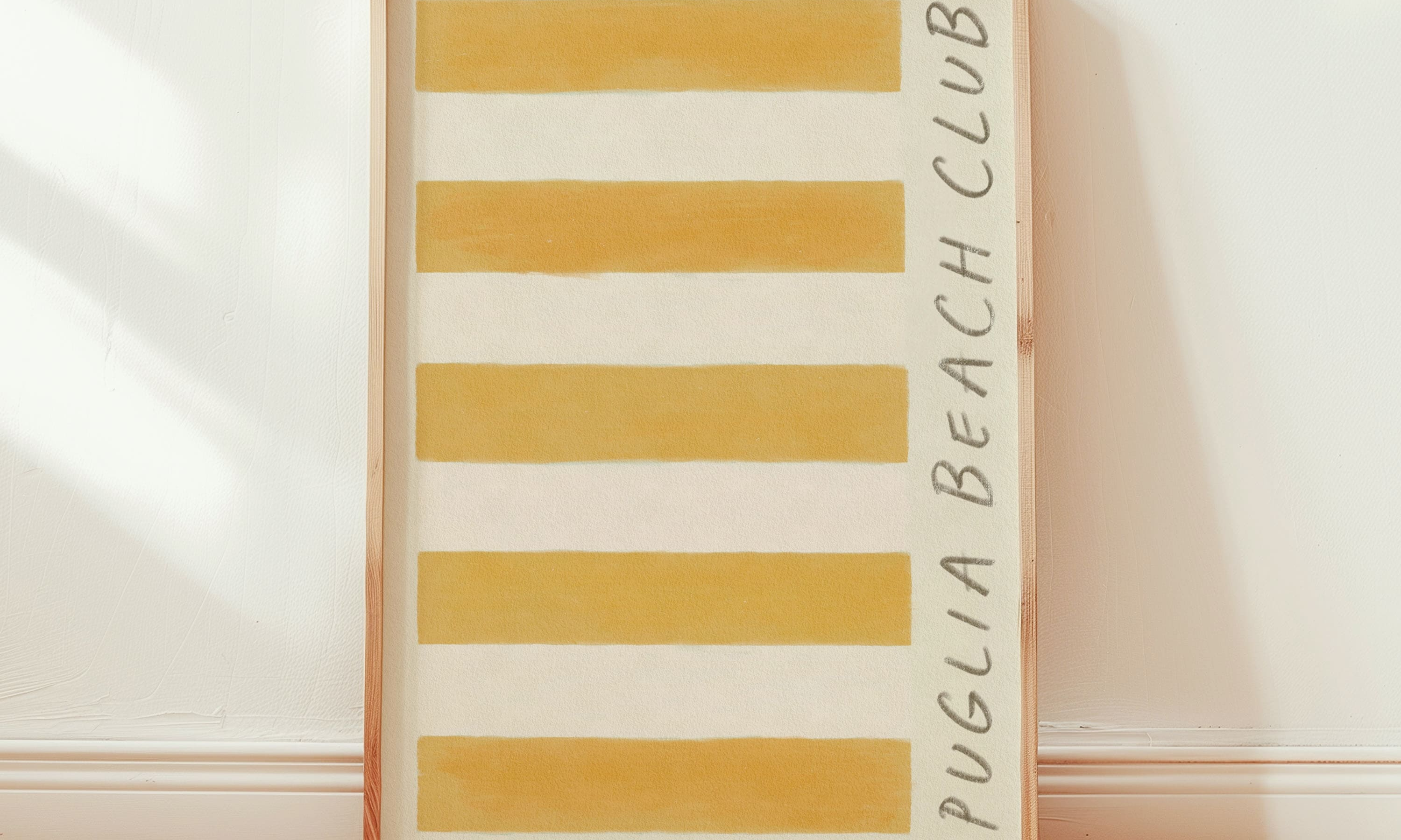 puglia beach club stripe giclee art print of original artist oil painting in a rich deep ochre yellow. This artwork is a replica of a retro stripe beach towel. Cotton paper Art print leans in a thin pine wood glass frame against Edward bummer white interior painted walls. The framed art print is positioned in a room bright from the sun, with rays shining through the bedroom window to the left.