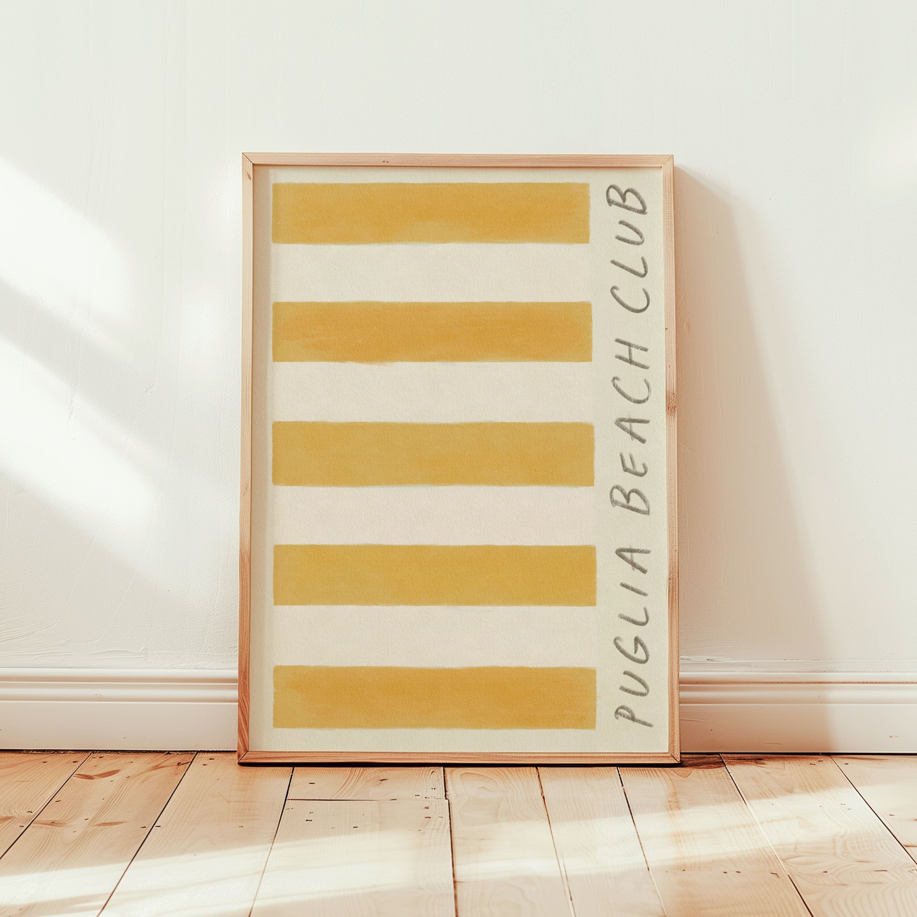 puglia beach club stripe giclee art print of original artist oil painting in a rich deep ochre yellow. This artwork is a replica of a retro stripe beach towel. Cotton paper Art print leans in a thin pine wood glass frame against Edward bummer white interior painted walls. The framed art print is positioned in a room bright from the sun, with rays shining through the bedroom window to the left.