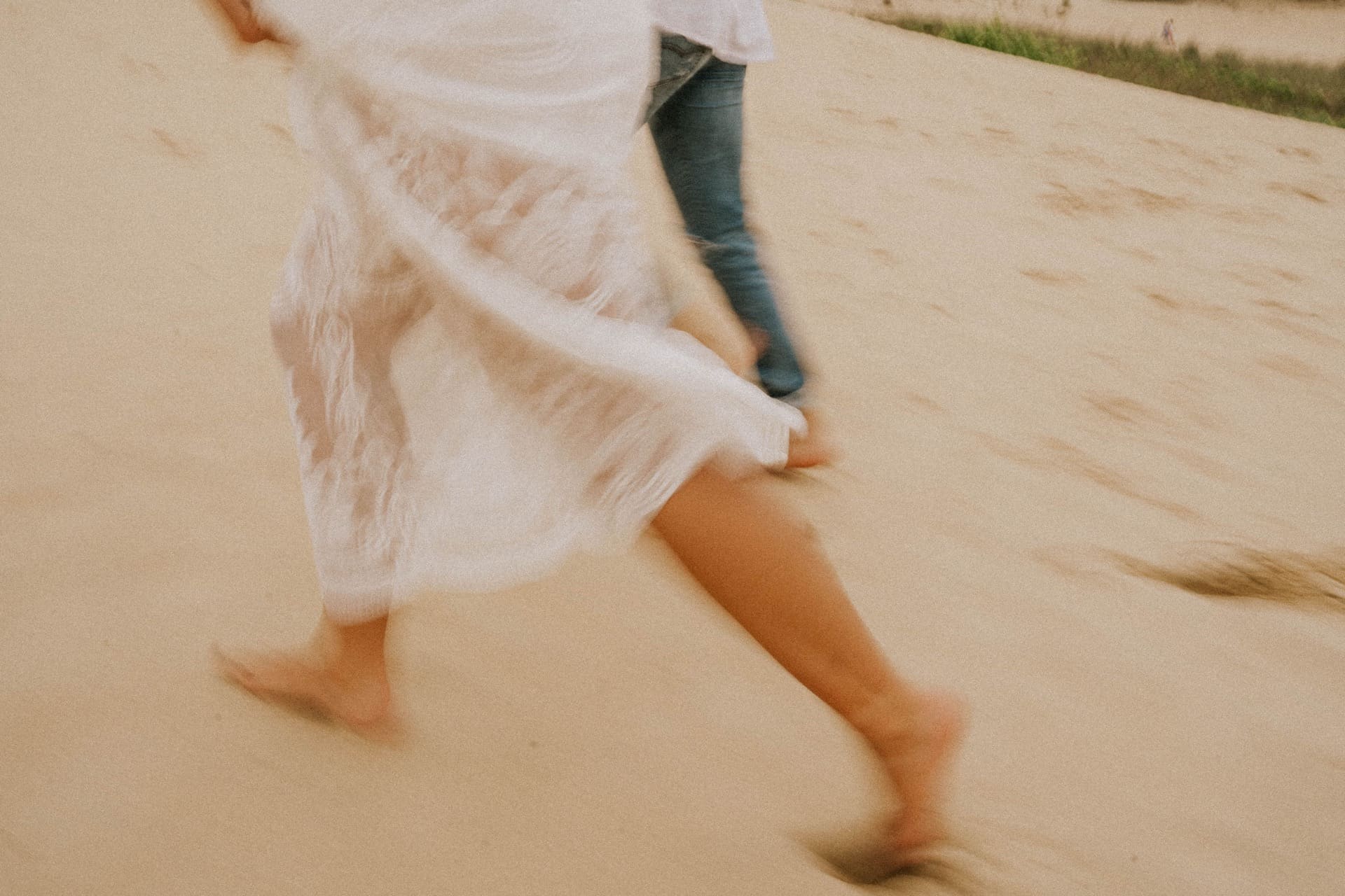 whimsically running across the sandy beach in white linen and cool denim, sinking into sand making foot prints